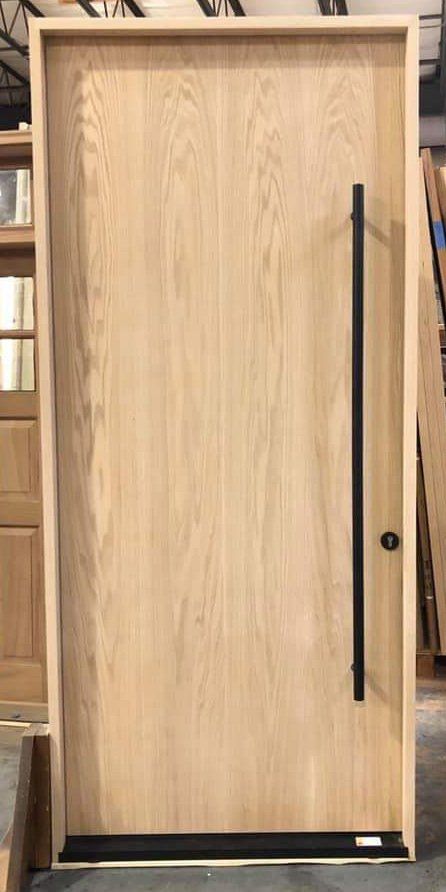 A wooden door with a black handle is sitting in a warehouse.