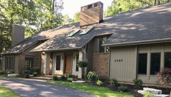 A large house with a driveway leading to it is surrounded by trees.
