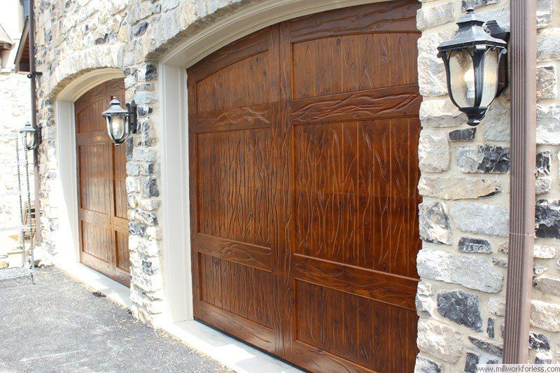 Two wooden garage doors are on a stone building.