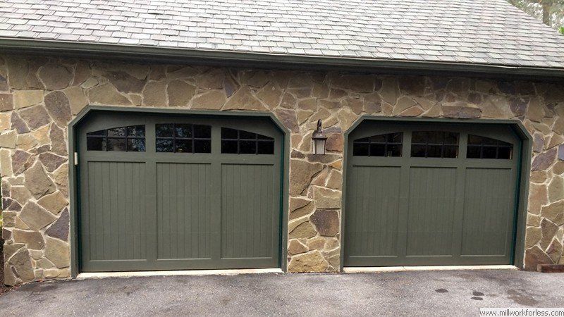 A garage with two green garage doors and a stone wall.