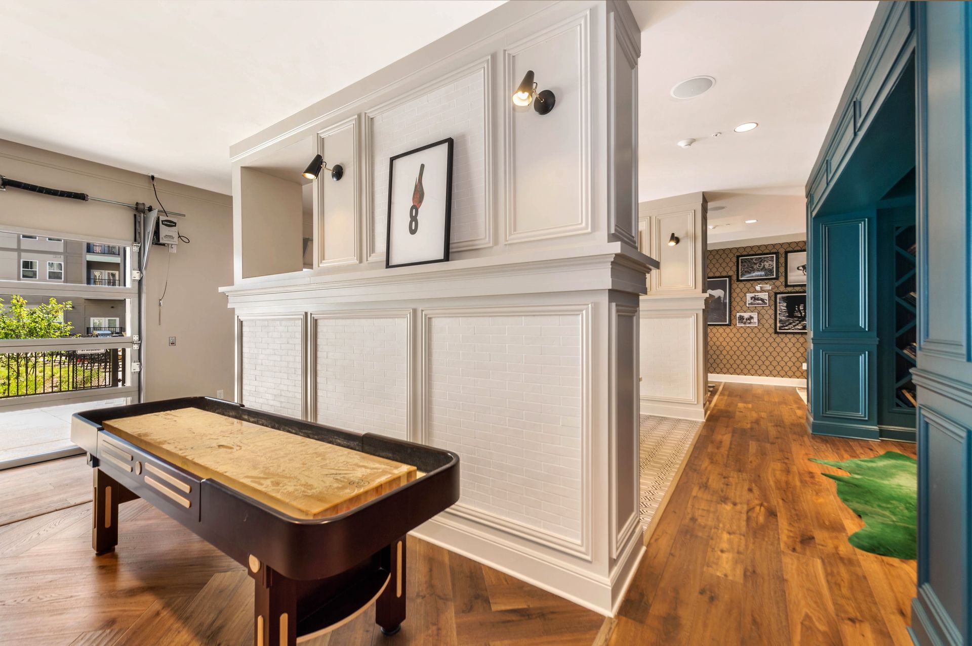 Interior view featuring a shuffleboard table, stylish wall paneling, and decorative lighting, with glimpses of a doorway leading to another room.