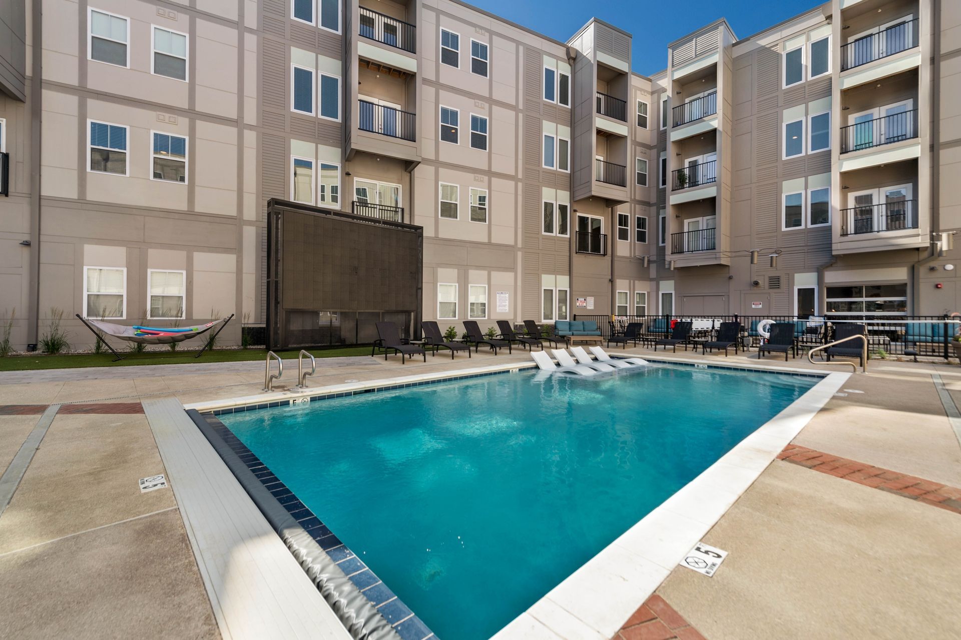 Outdoor swimming pool surrounded by lounge chairs and an apartment building.