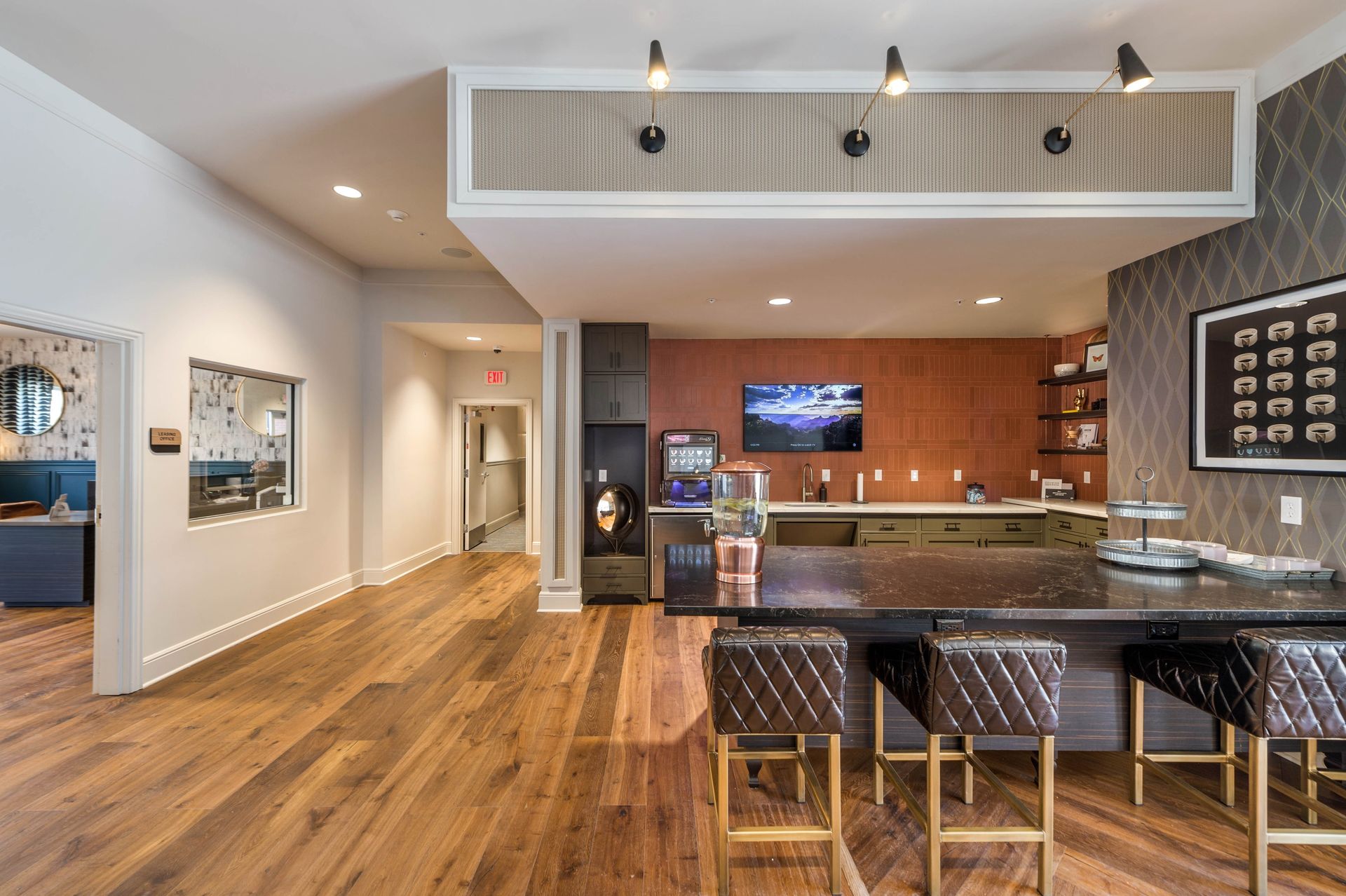 Modern lounge area featuring a dark countertop with bar stools, a wall-mounted TV, and a beverage station, complemented by warm wood floors and stylish decor.