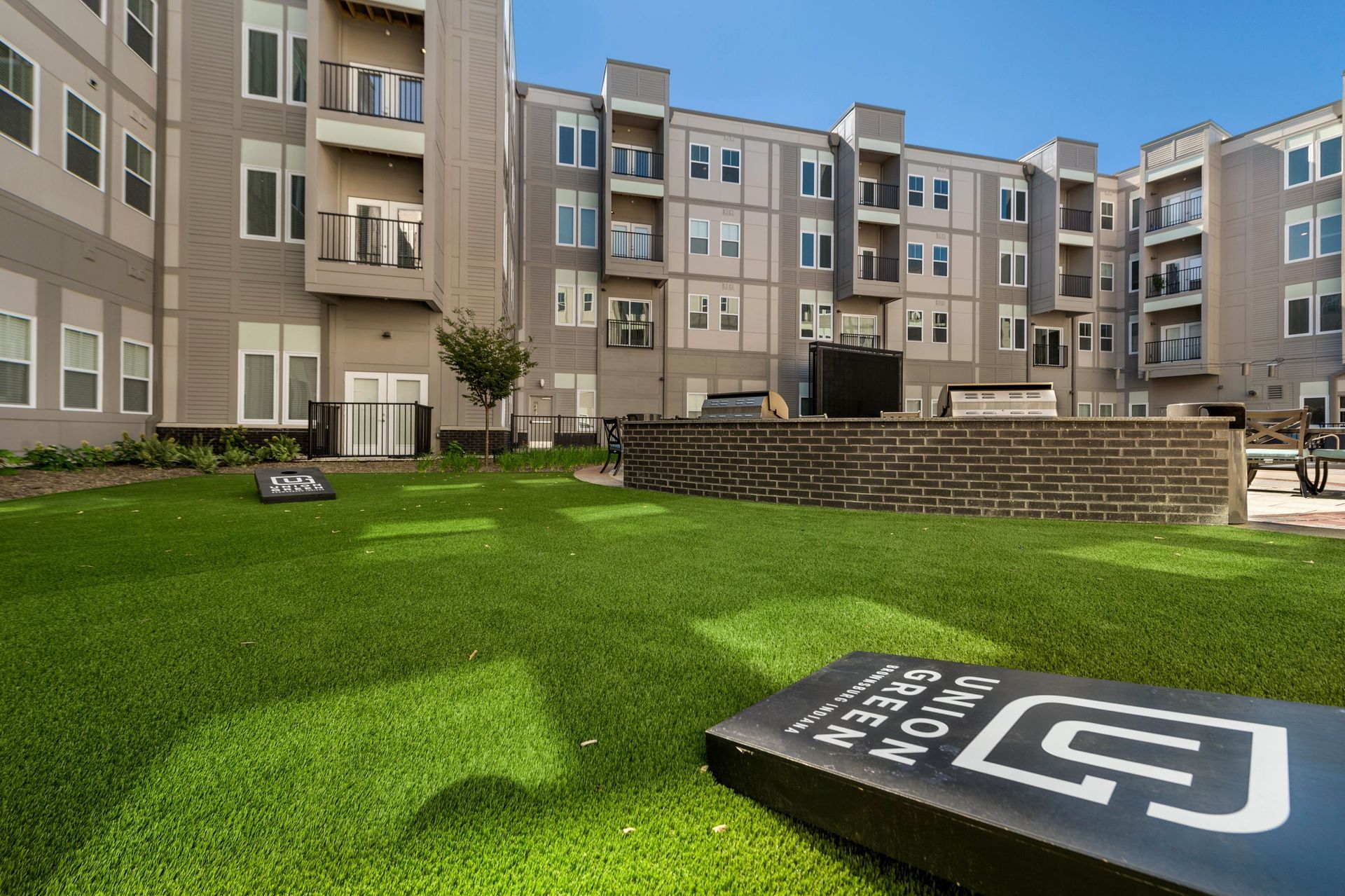View of a landscaped courtyard with artificial turf and modern apartment buildings in the background.