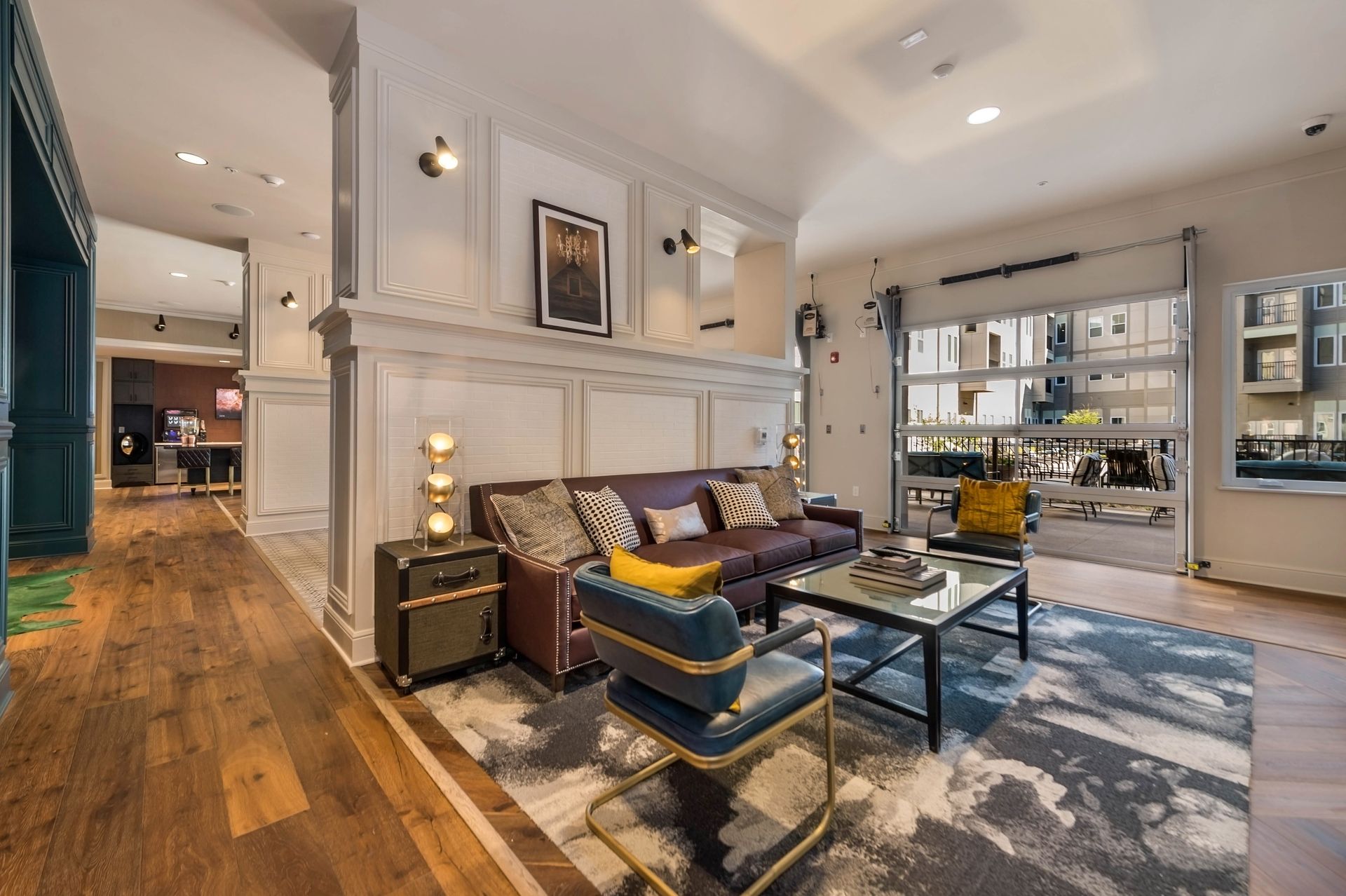 A cozy interior space featuring a modern sofa with decorative cushions, a coffee table, and stylish accent chairs, complemented by wooden flooring and natural light from large windows.