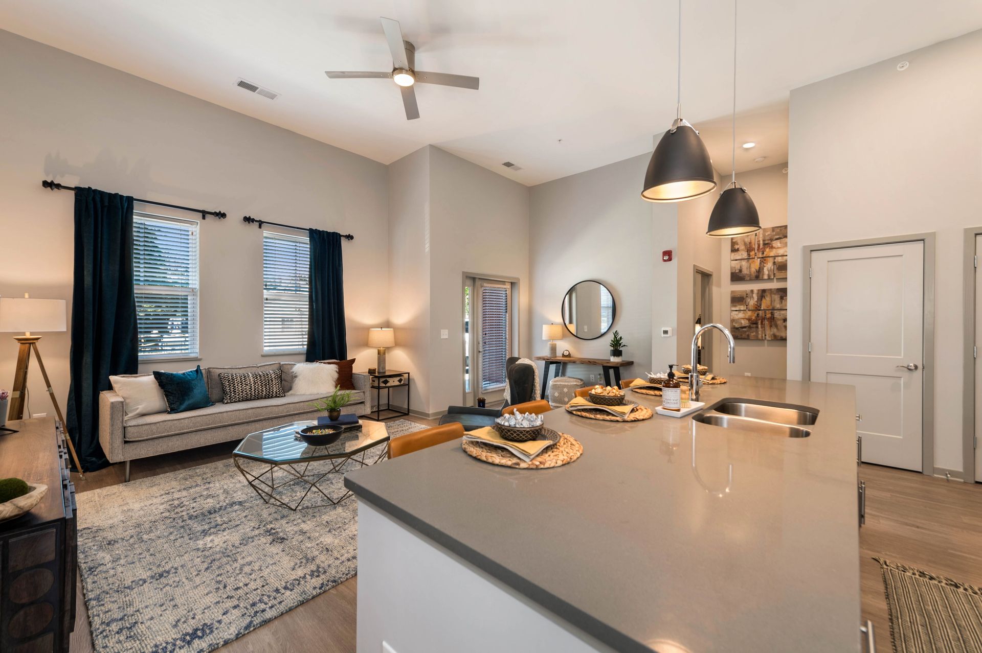 Modern living room and kitchen area with a comfortable sofa, coffee table, and dining space, featuring large windows and stylish decor.
