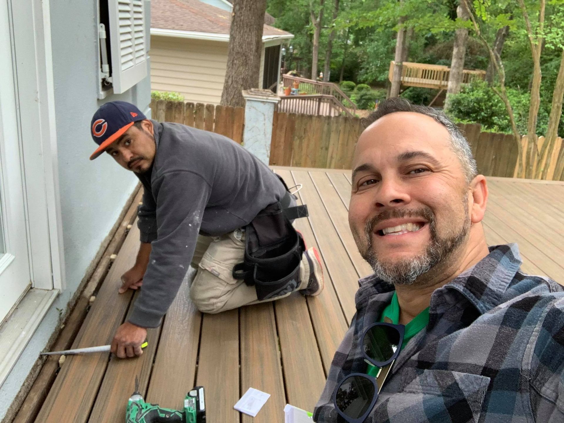 Two men are working on a deck and smiling for the camera.