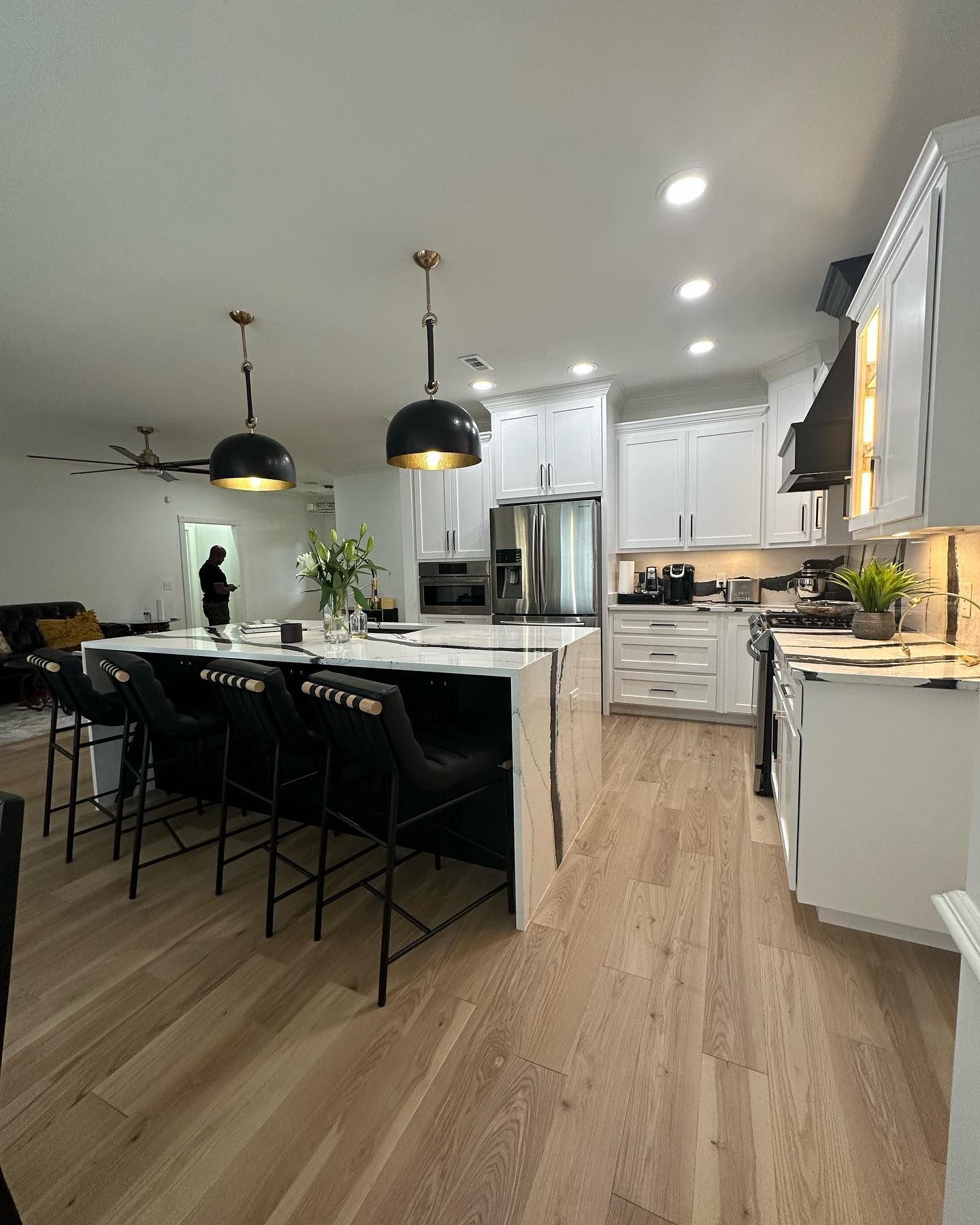 A kitchen with white cabinets , hardwood floors , and a large island.