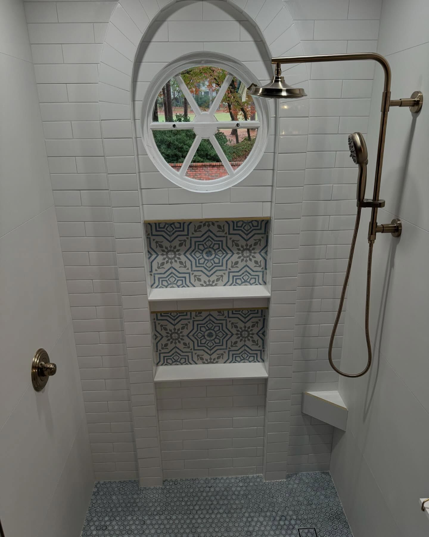 A shower with a round window and a shower head.
