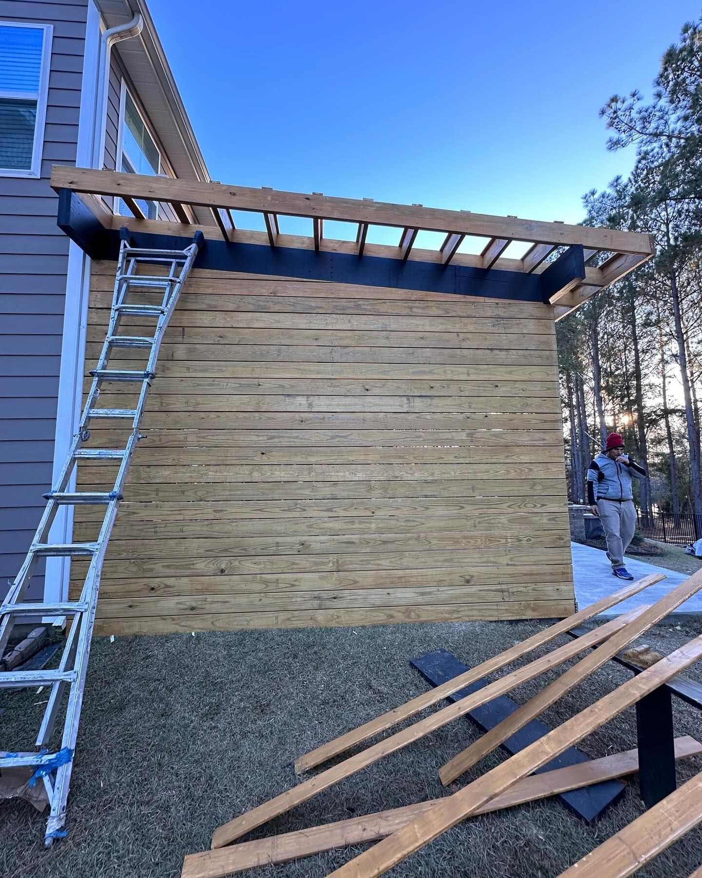 A ladder is sitting next to a wooden wall in front of a house.