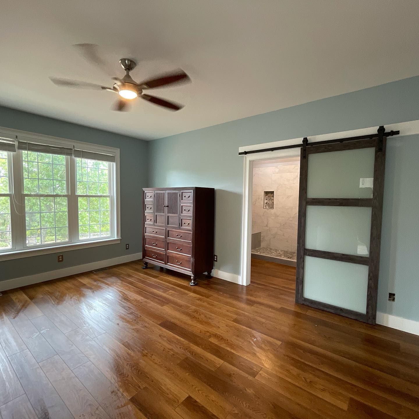 A living room with hardwood floors , a ceiling fan , a dresser and a sliding barn door.