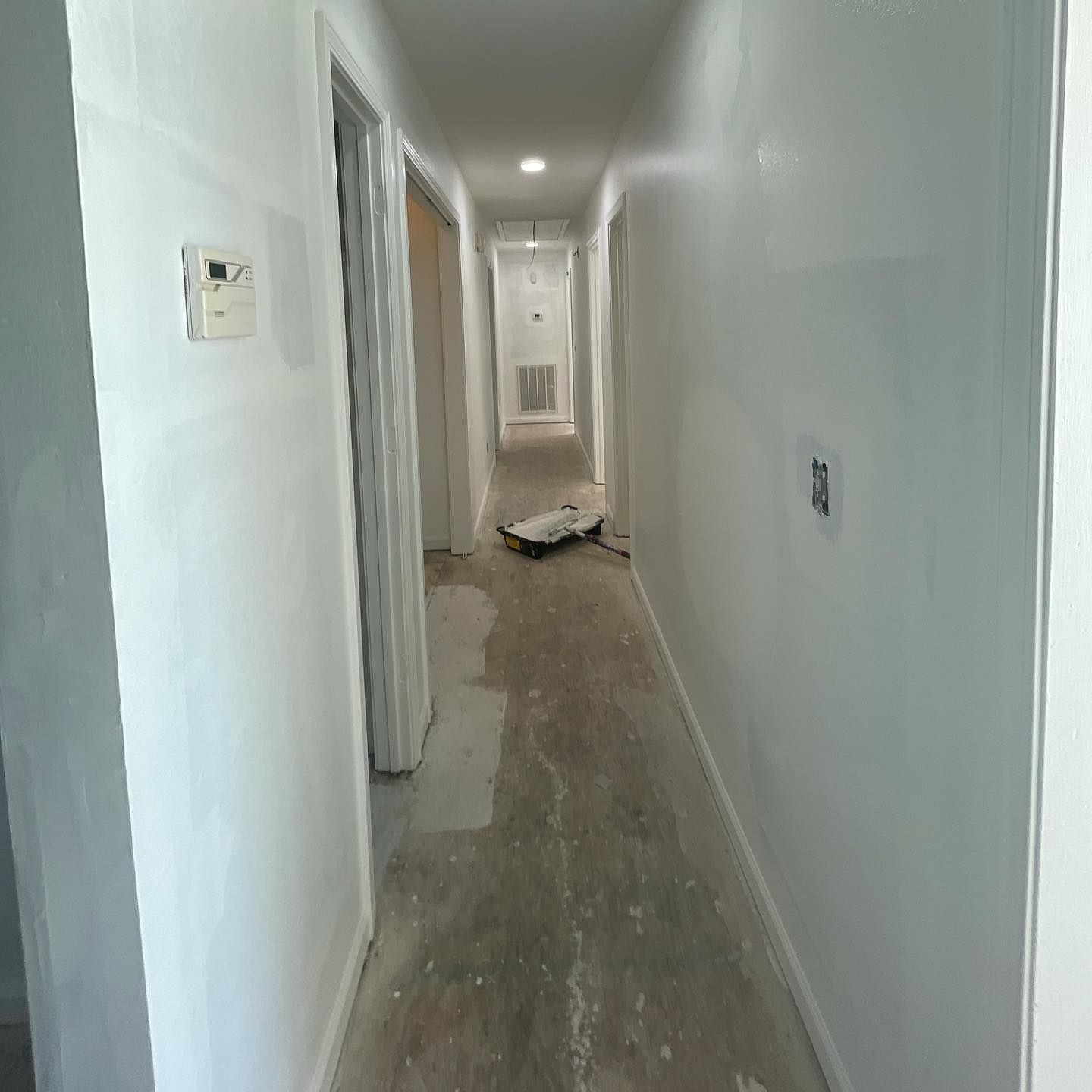 A long hallway with white walls is being painted.