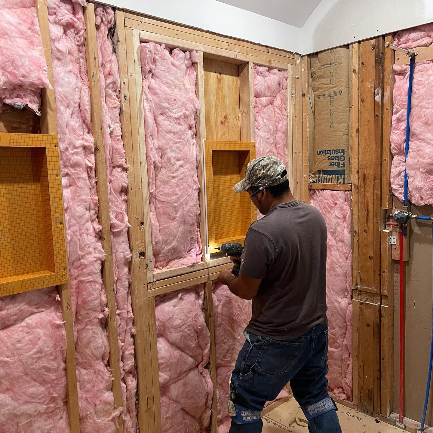 A man is working on a wall with pink insulation.