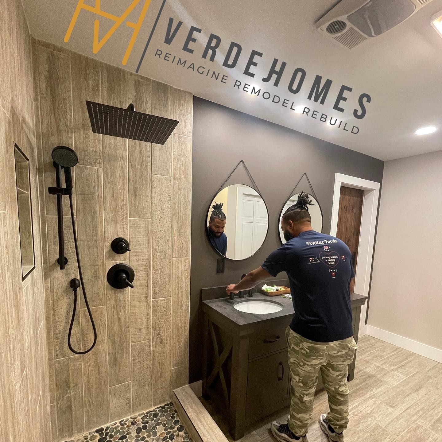 A man is standing in a bathroom next to a sink and shower.