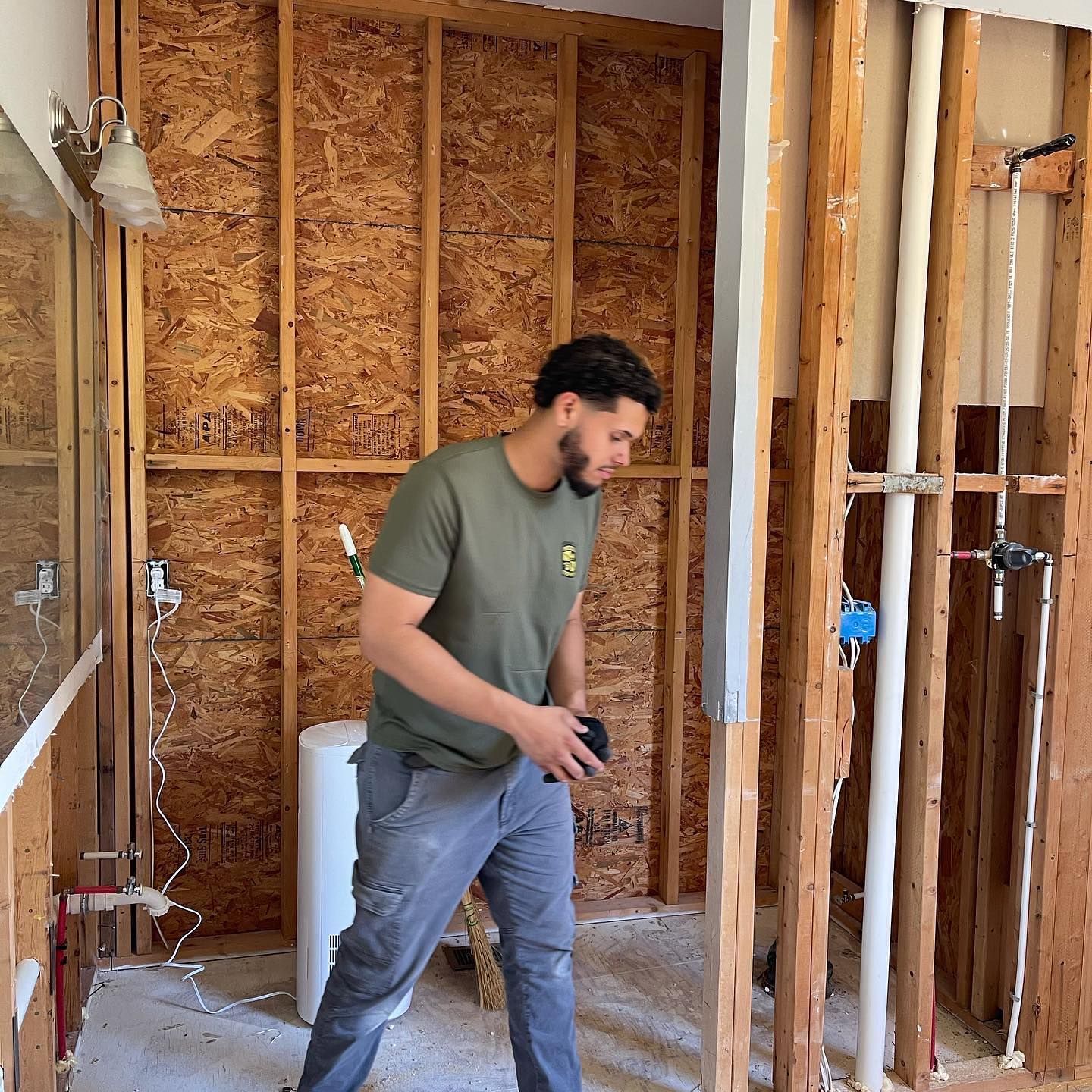 A man in a green shirt is standing in a bathroom under construction.