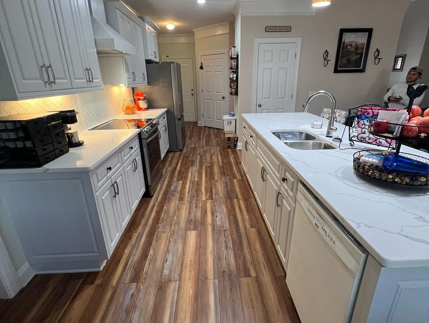 A kitchen with hardwood floors , white cabinets , a sink , and a refrigerator.