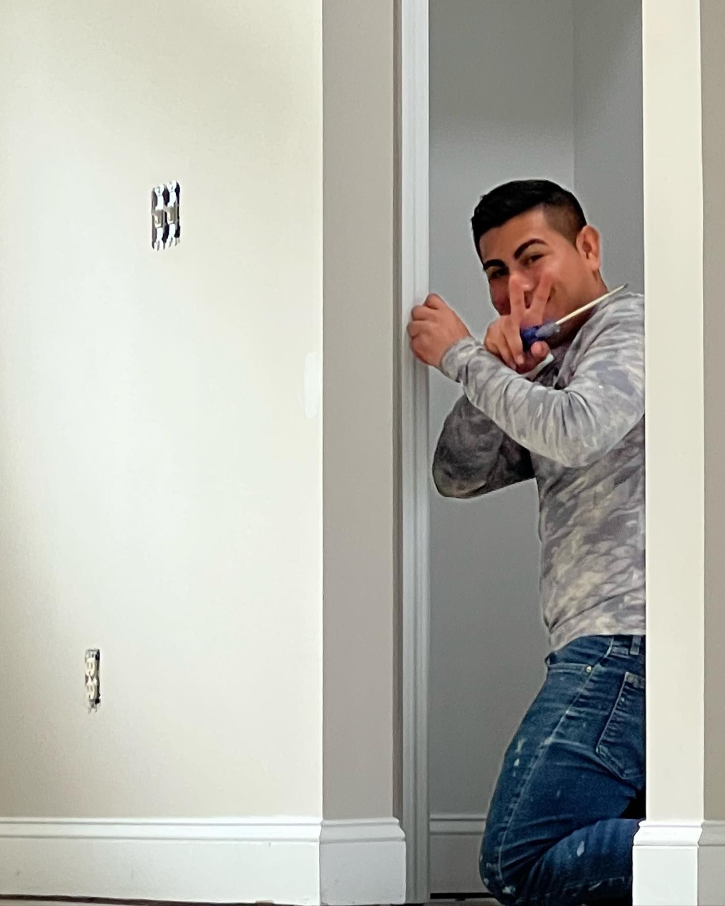 A man is kneeling down in a room holding a screwdriver.