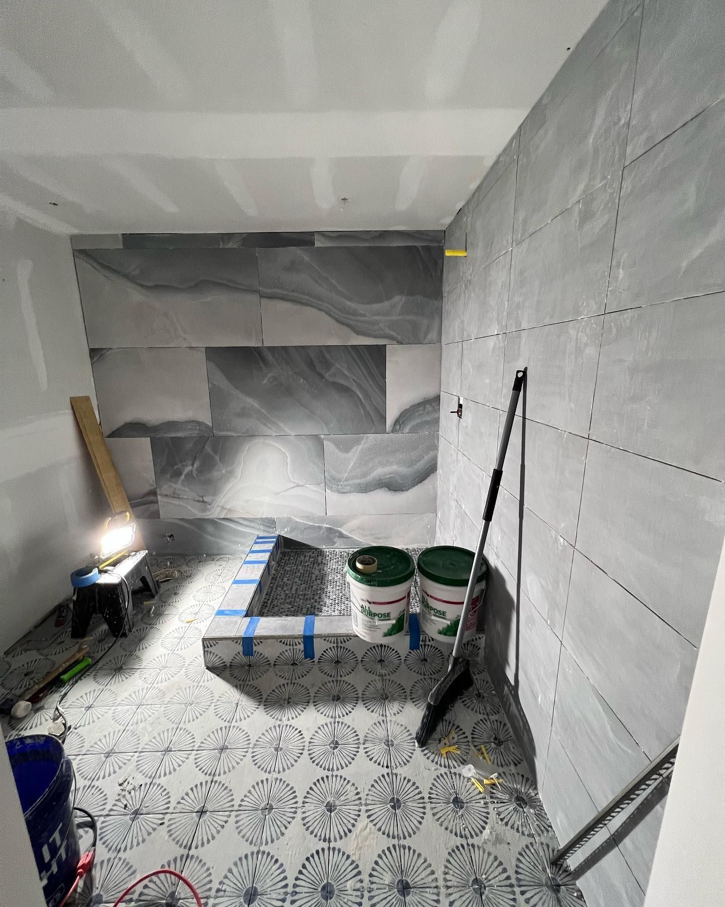 A bathroom under construction with buckets and a mop on the floor.