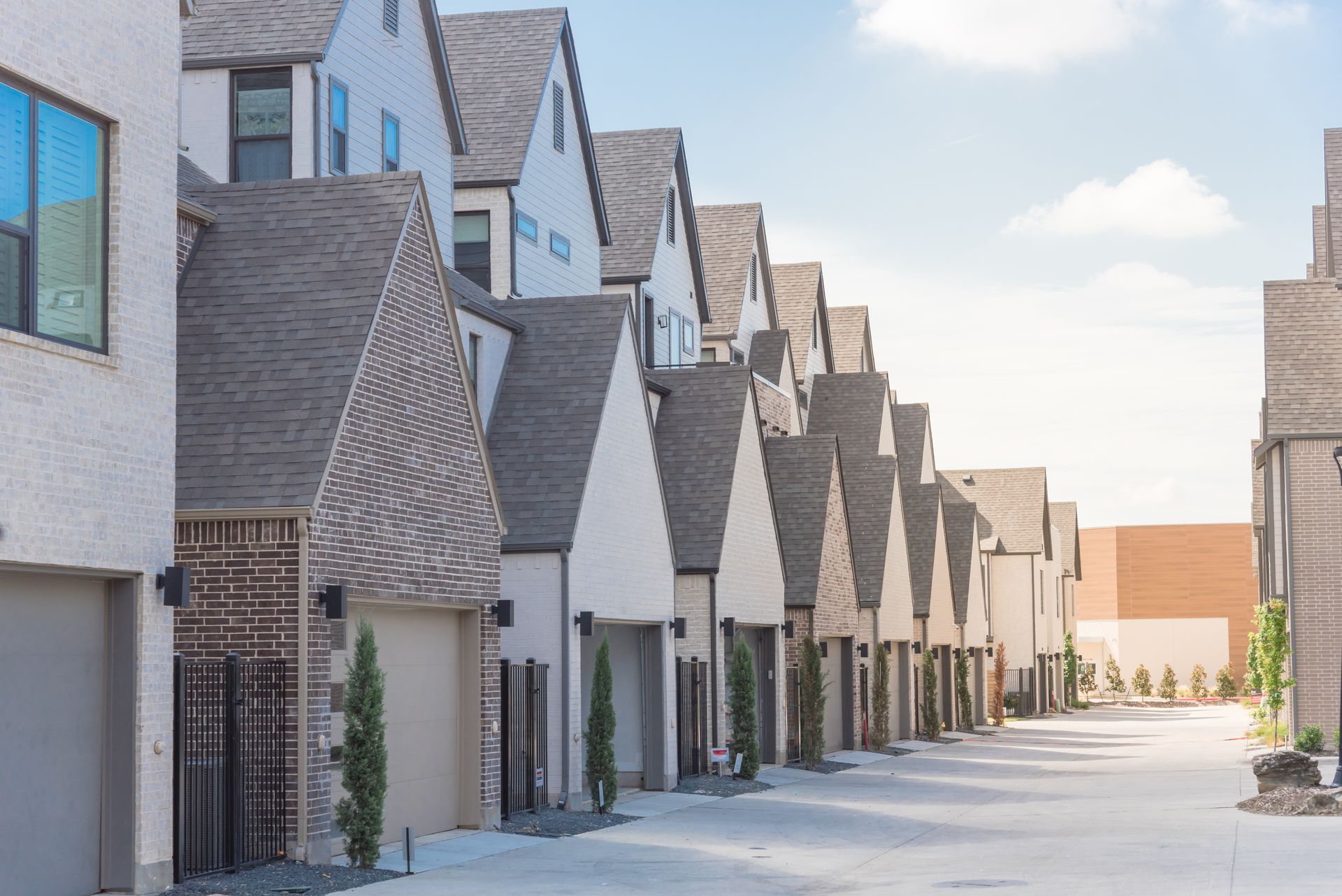 Row of modern townhouses with gabled roofs and attached garages along a sunny street.