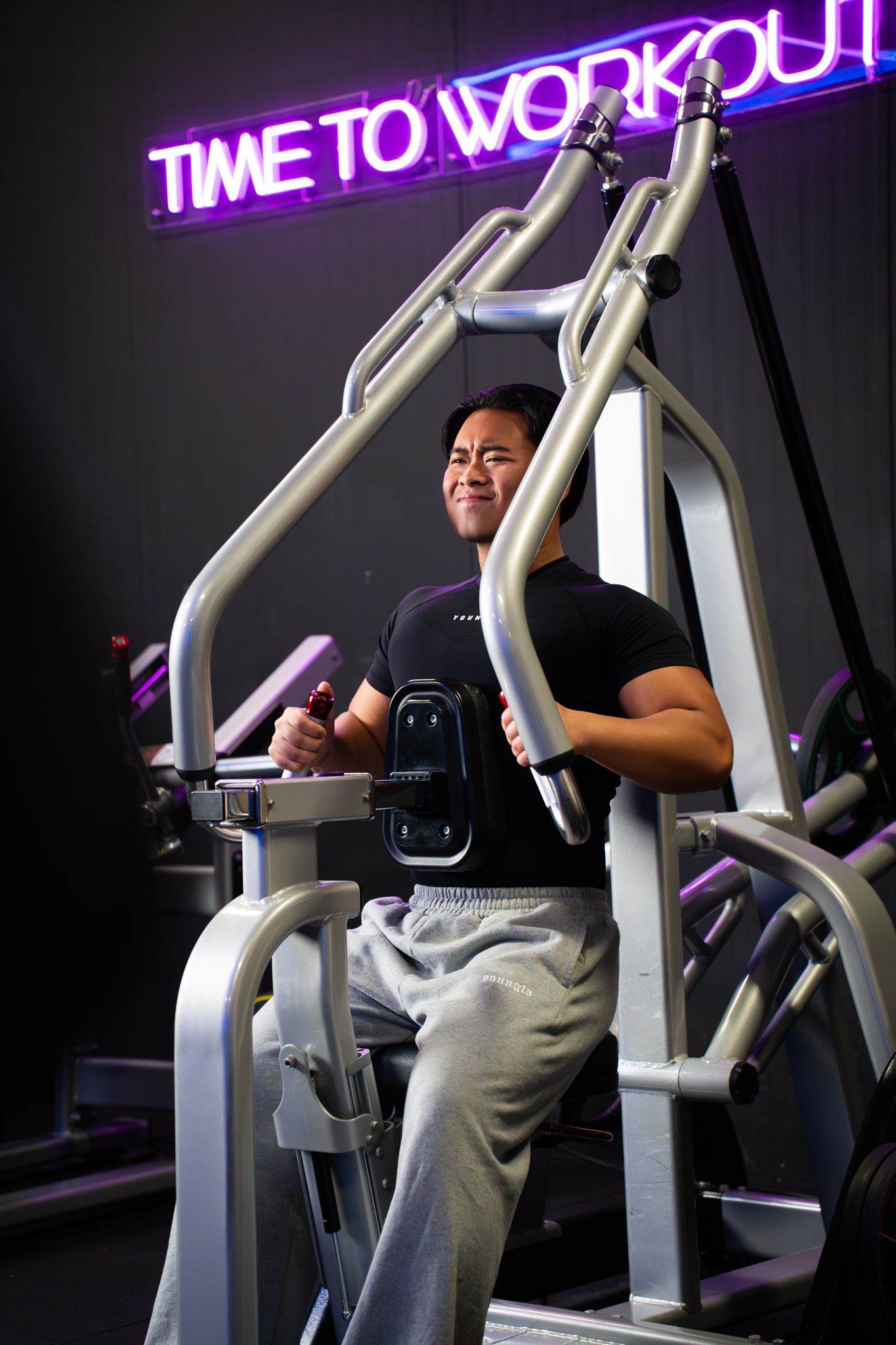 Persoon staat op een fitnessapparaat onder een neonbord met de tekst 