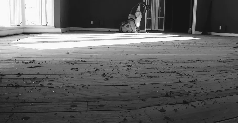 A black and white photo of a wooden floor in an empty room.