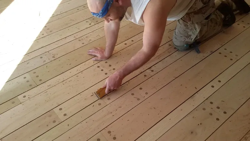 A man is cleaning a wooden floor with a brush.