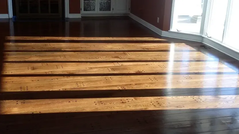 The sun is shining through the windows on a wooden floor in a living room.