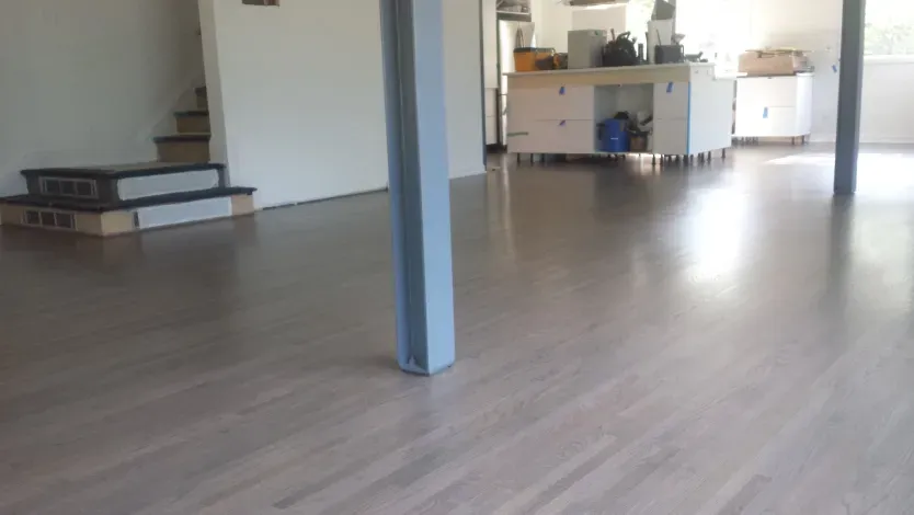 A large empty room with a wooden floor and stairs.