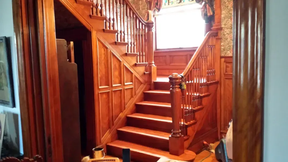 A wooden staircase in a house with a cat sitting on the floor.