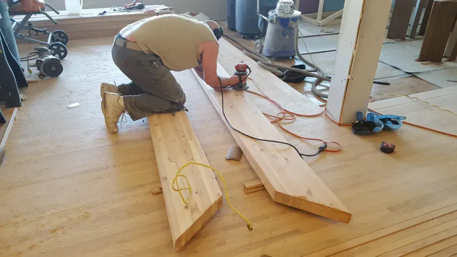 A man is kneeling down while working on a piece of wood.