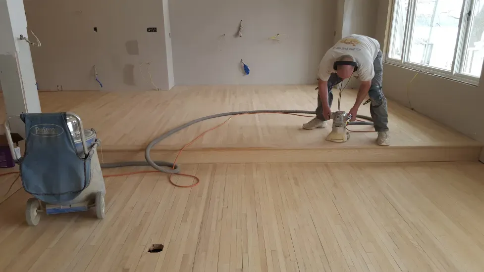 A man is sanding a wooden floor with a vacuum cleaner.