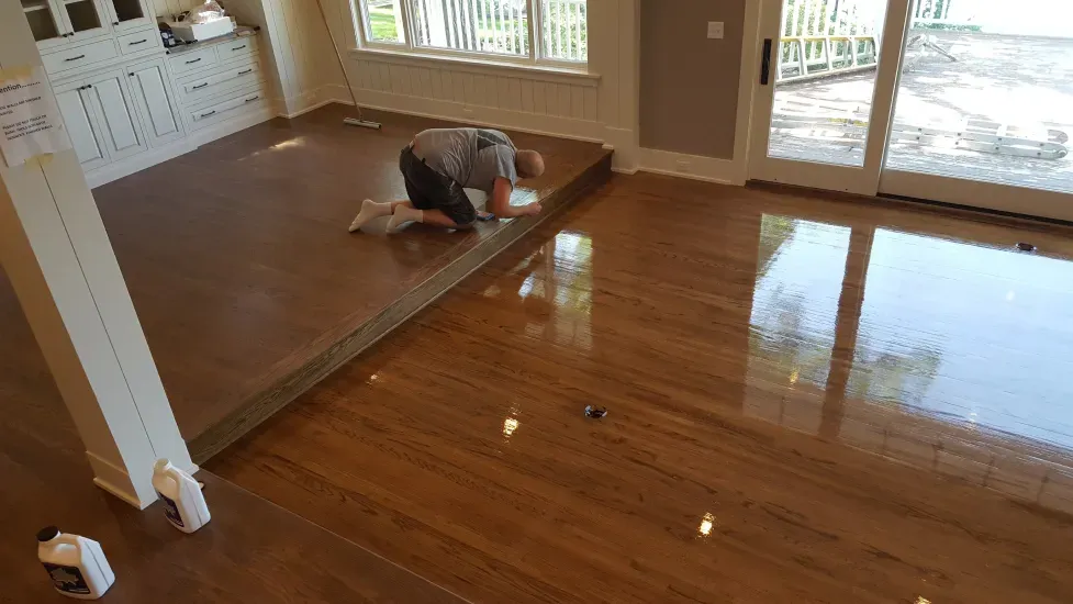 A man is kneeling on a wooden floor in a living room.