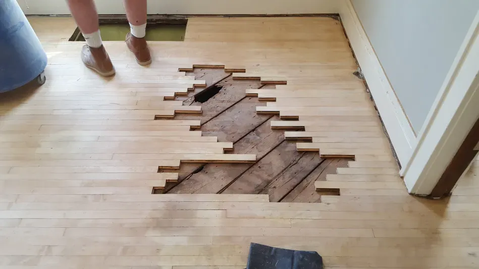 A person is standing on a wooden floor with a hole in it.