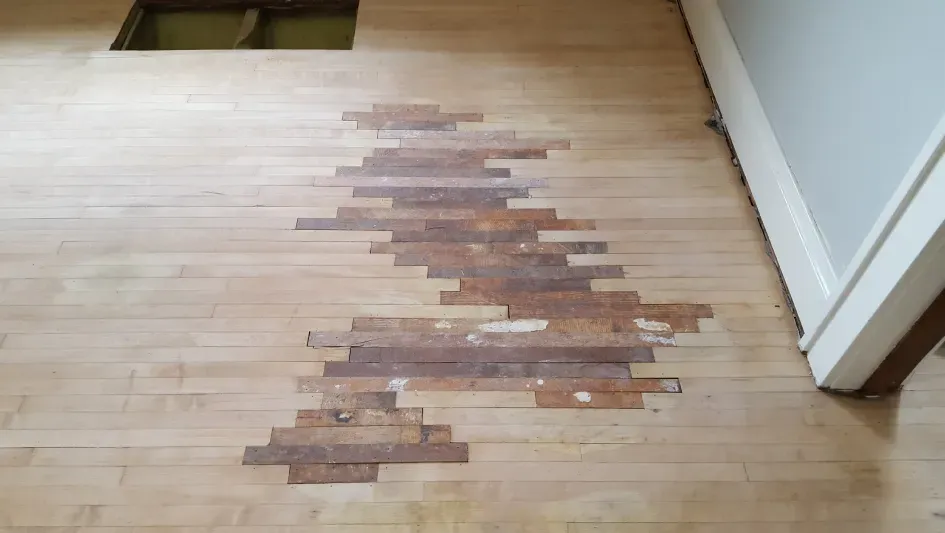 A wooden floor with a hole in it and a door in the background.