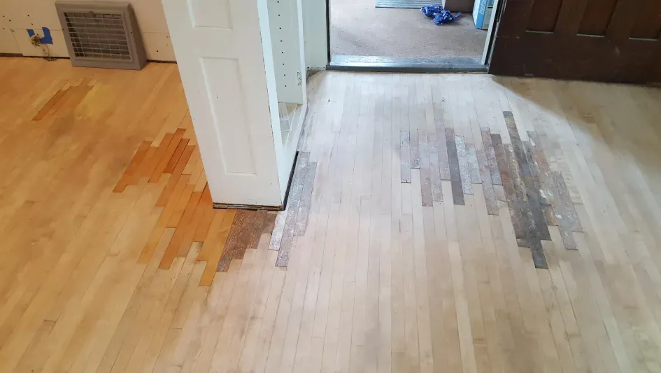 A wooden floor is being restored in a living room.