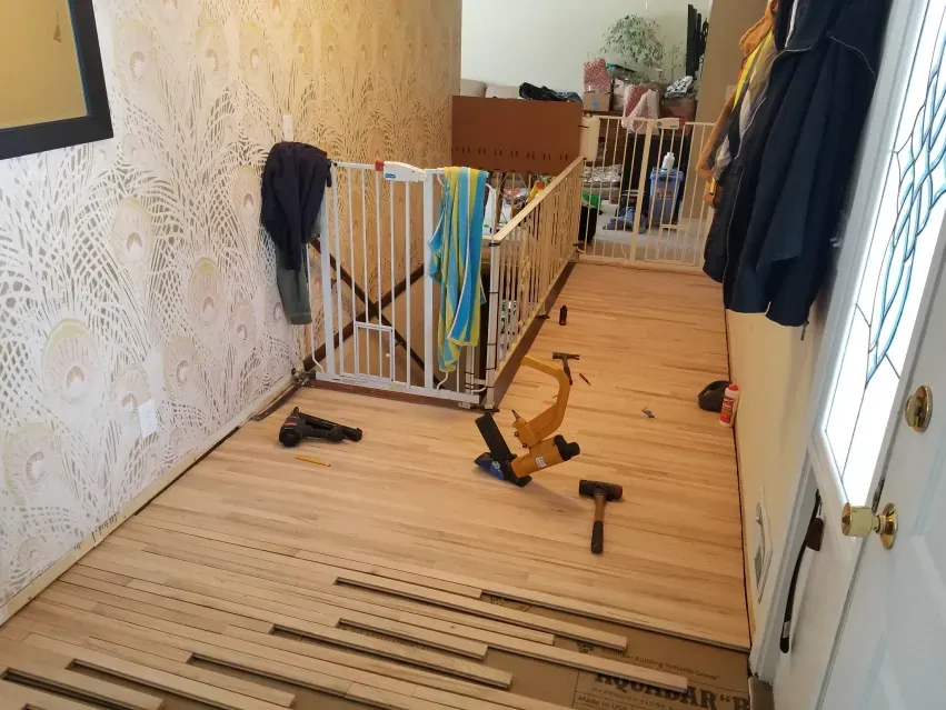 A wooden floor is being installed in a room with a staircase.