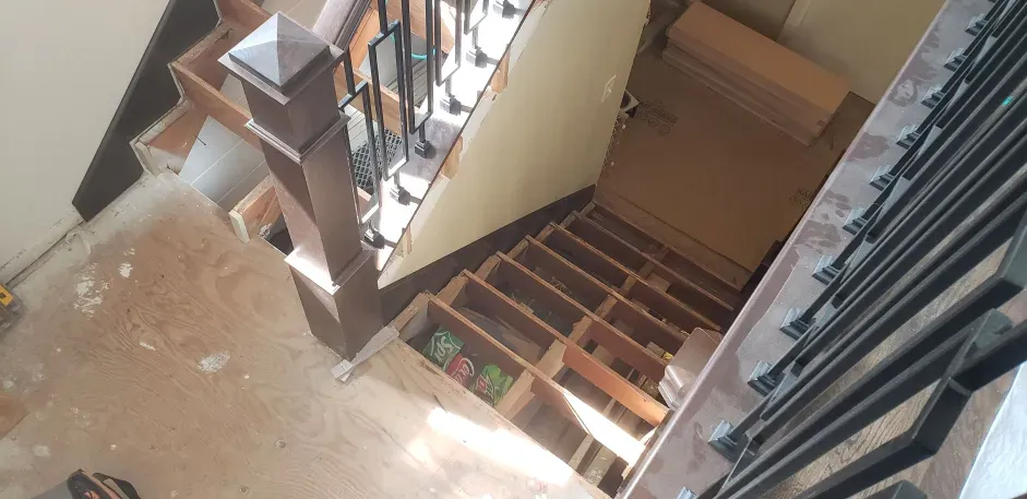 A wooden staircase with a metal railing is being built in a house.