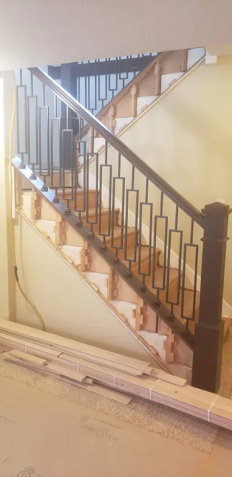 A wooden staircase with a metal railing is being built in a house.