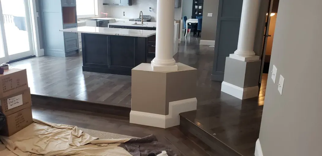 A living room with hardwood floors and a kitchen in the background.