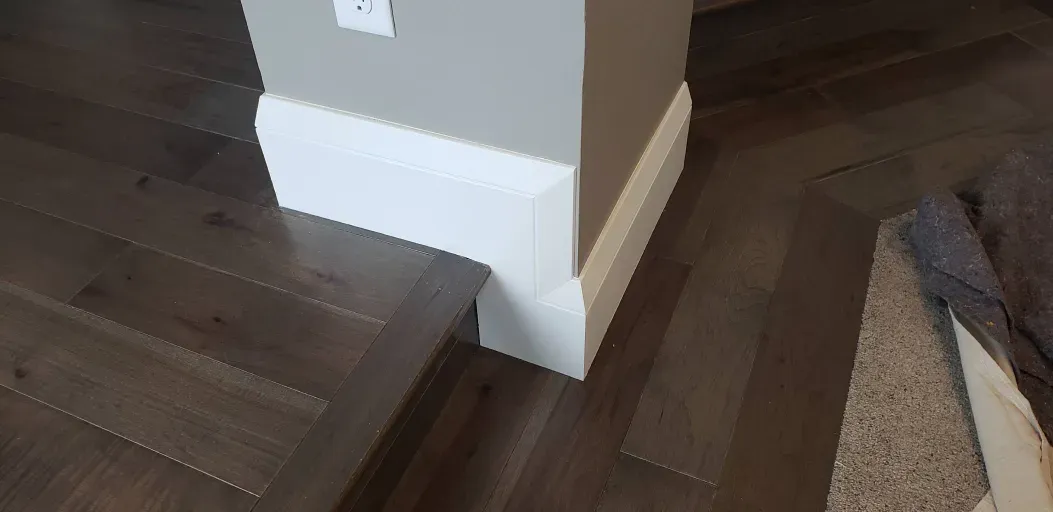 A close up of a wooden floor in a room with a white trim.