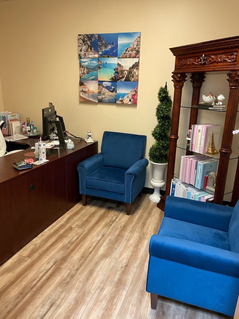 A waiting room with two blue chairs and a painting on the wall.