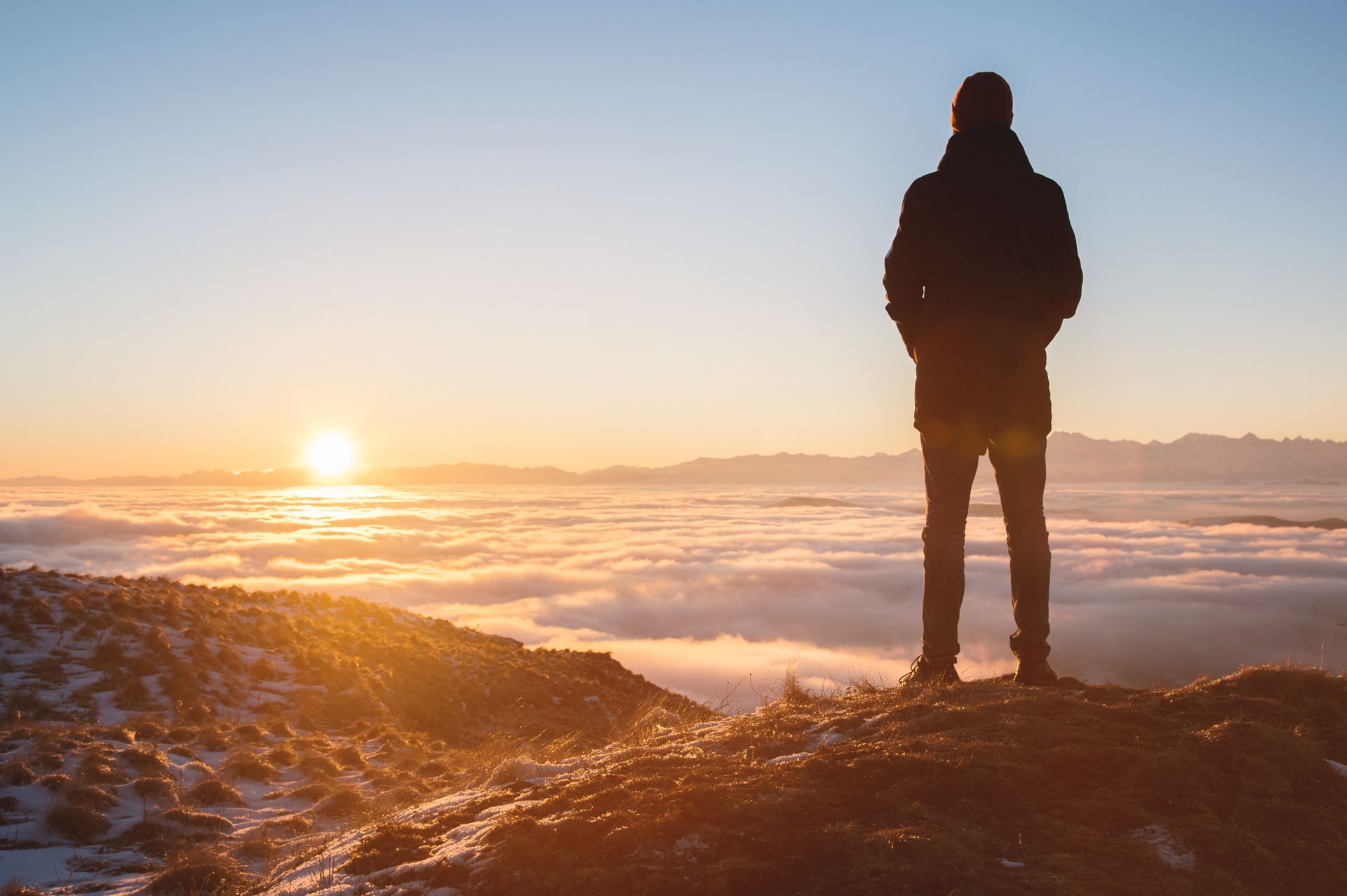 Man standing on a mountaintop, looking at a sunrise over a sea of clouds.
