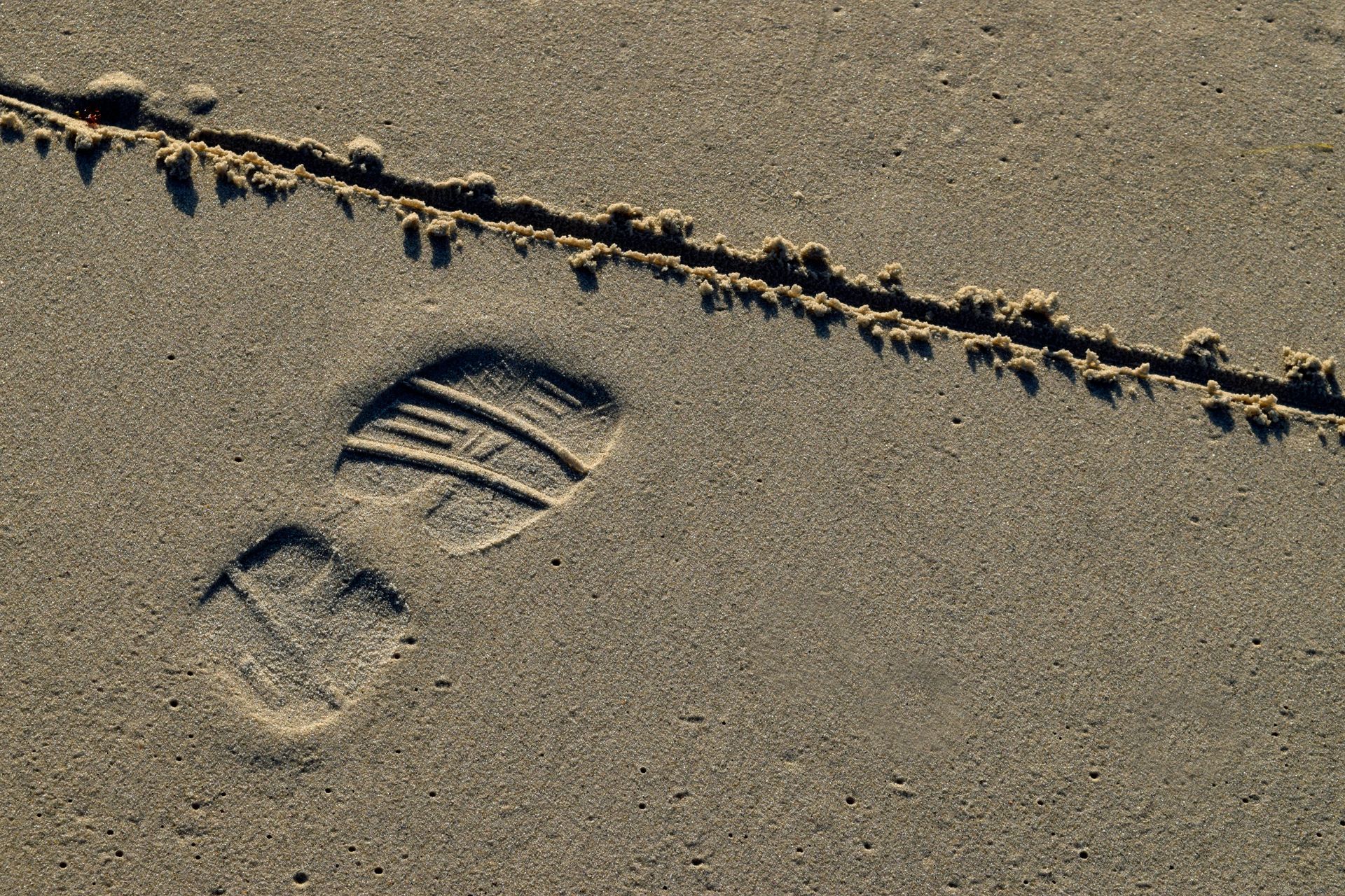 A close-up of a footprint in the sand on a beach with a line drawn on front of it