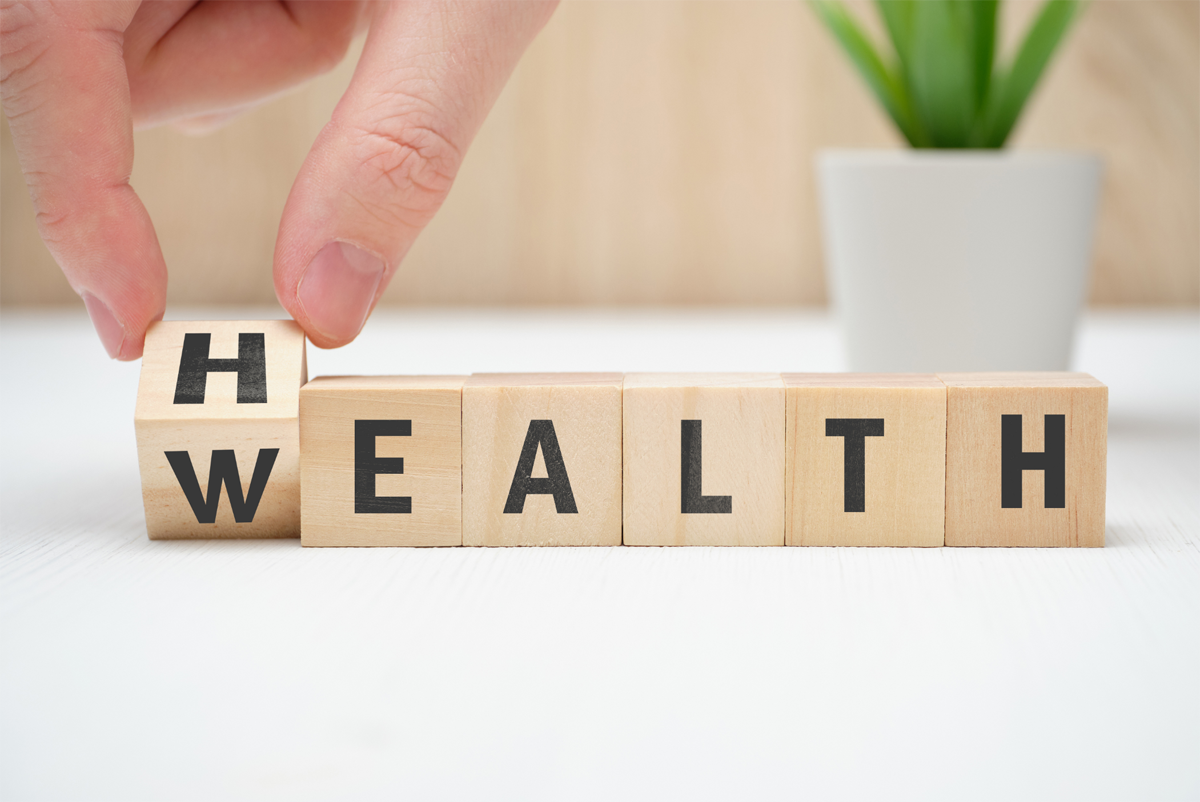 Wooden letter blocks spelling Health, with a person rotating the H block to reveal a W, changing the word to Wealth