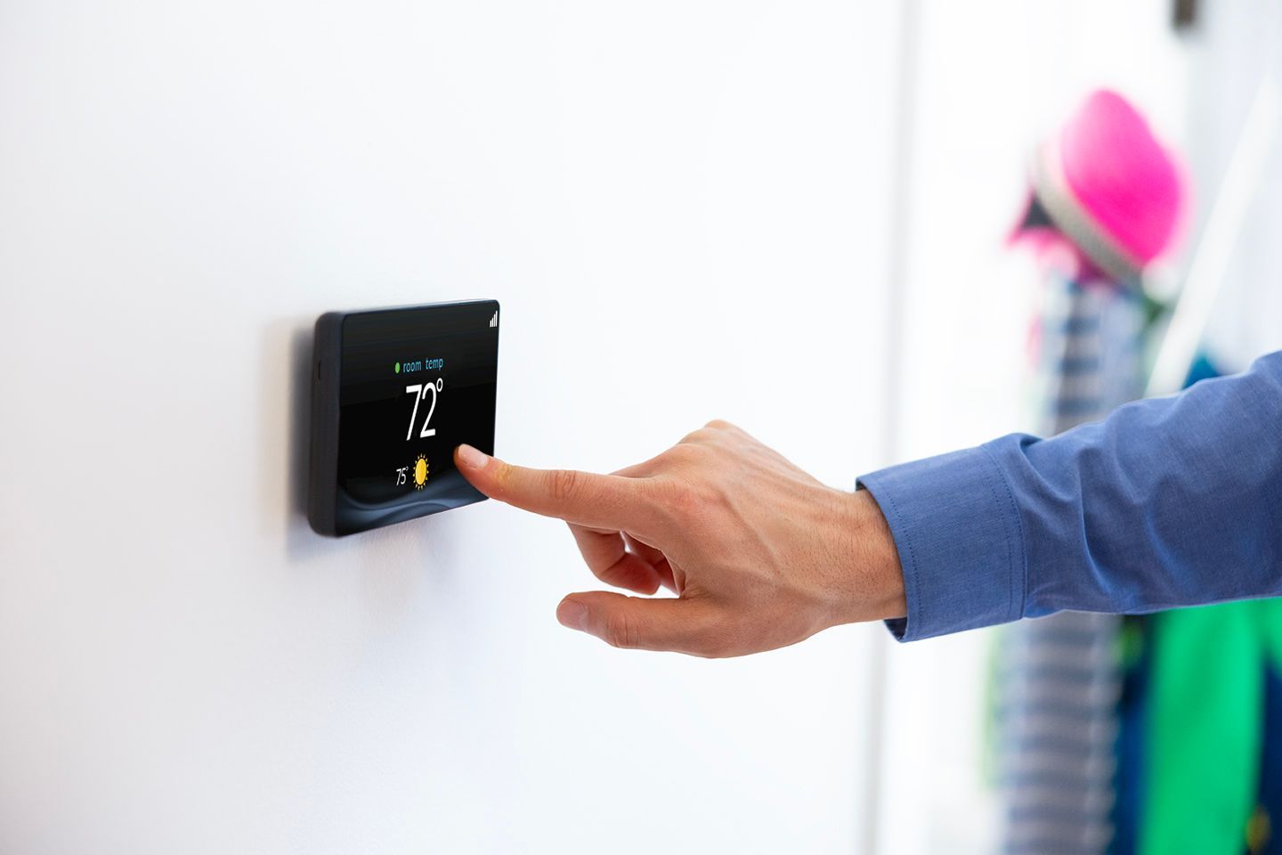 Hand adjusting a wall-mounted thermostat on a white wall