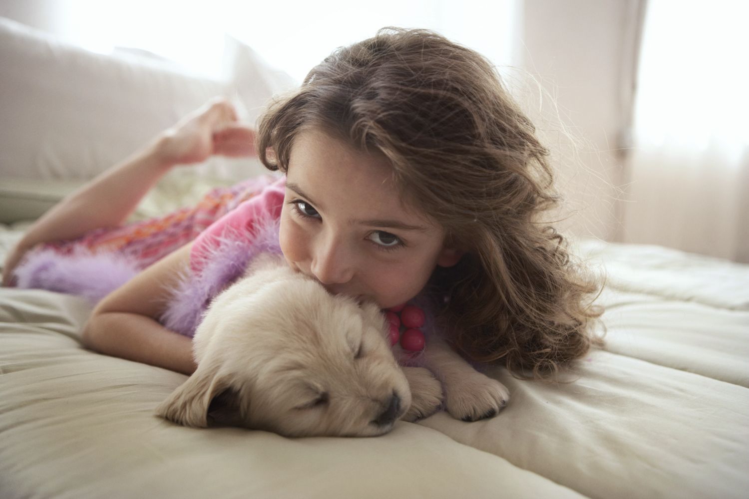 Child lying on a bed cuddling a sleeping puppy in soft daylight