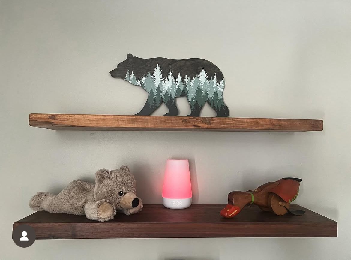 A wooden shelf with a bear , a stuffed animal , and a lamp on it.