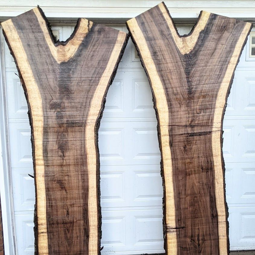 Two dark wood slabs with live edges stand upright against a white garage door. The wood has a light colored sapwood border.