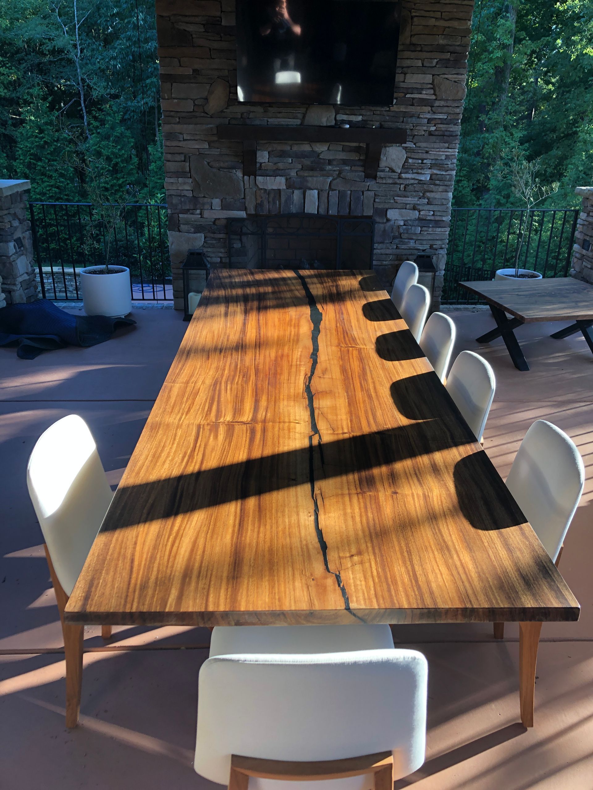 A long wooden table with white chairs in front of a stone fireplace.
