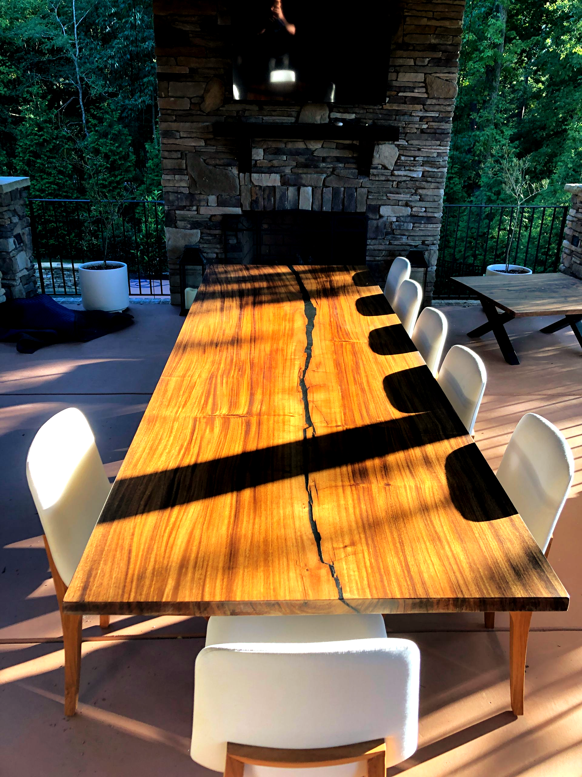 Custom Outdoor dining table with white chairs, stone fireplace, and sunny patio.